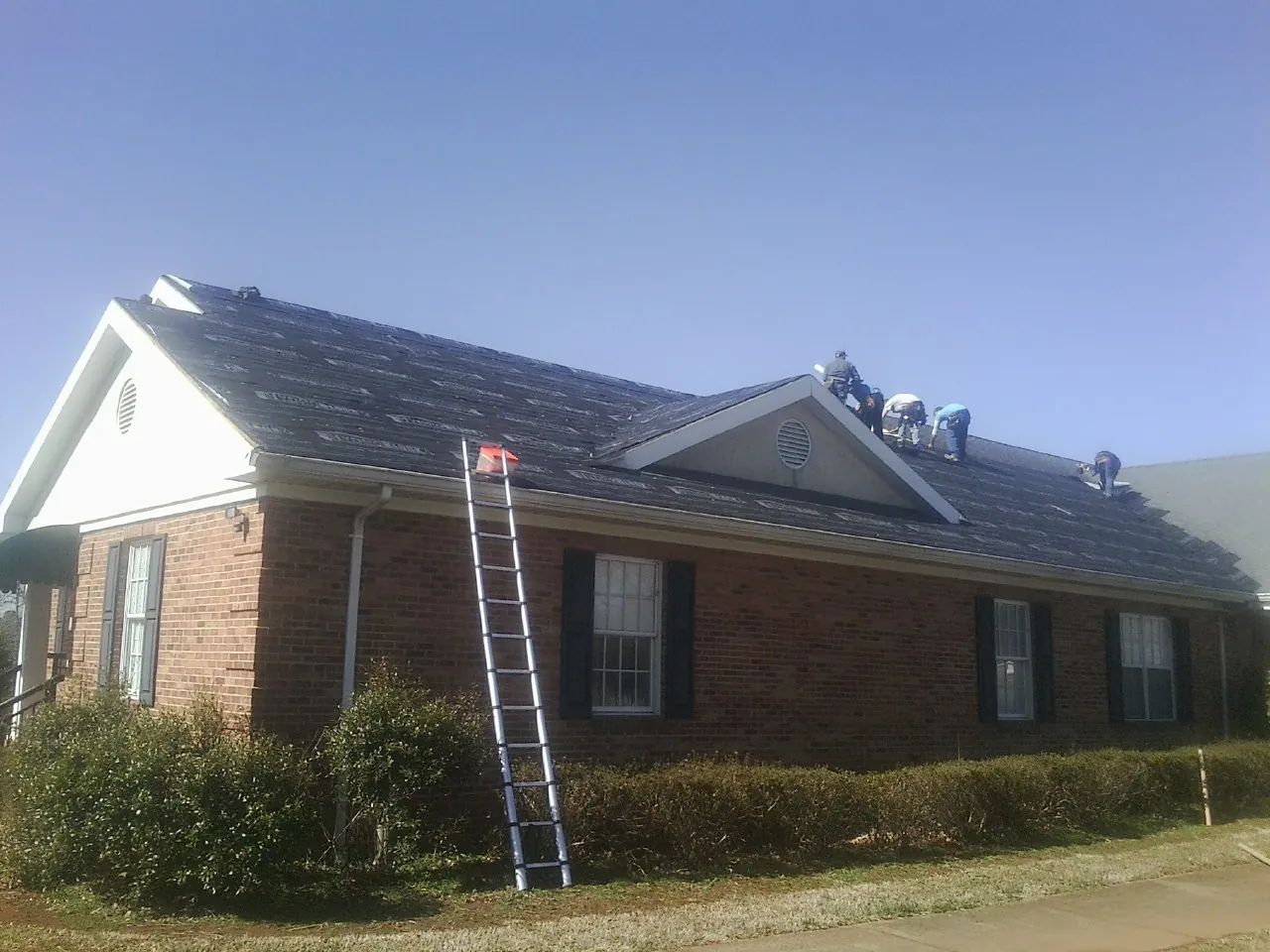 Crew tearing shingles off a brick ranch roof with a ladder set — Metal Roof Repair work by our crew in Rex