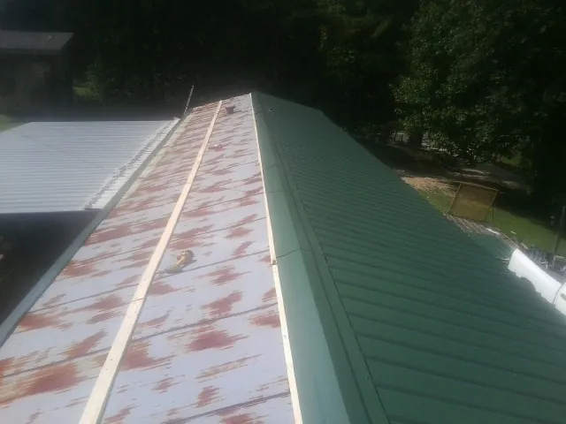 Old rusted panels beside newly installed green metal roofing — Wind Damage Roof Repair by Roofing Brothers in Rex