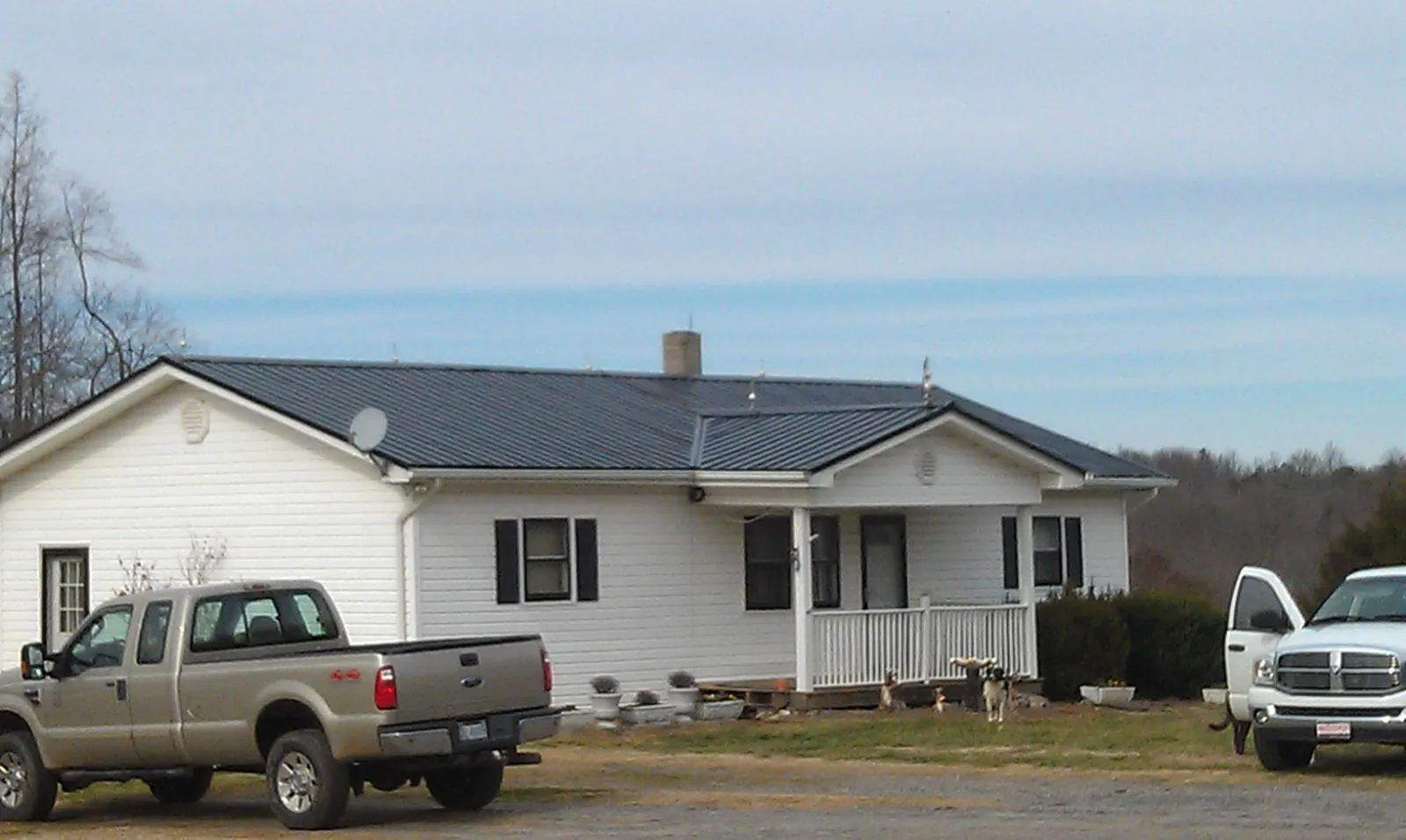 Finished dark metal roof on a white ranch home with work trucks parked in Rex