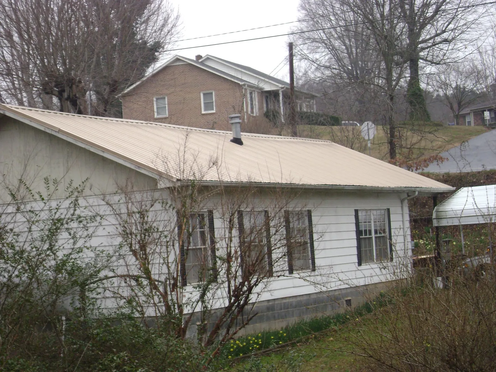 Tan metal roof on a white sided house set into a hillside — Commercial Roofing by Roofing Brothers in Rex