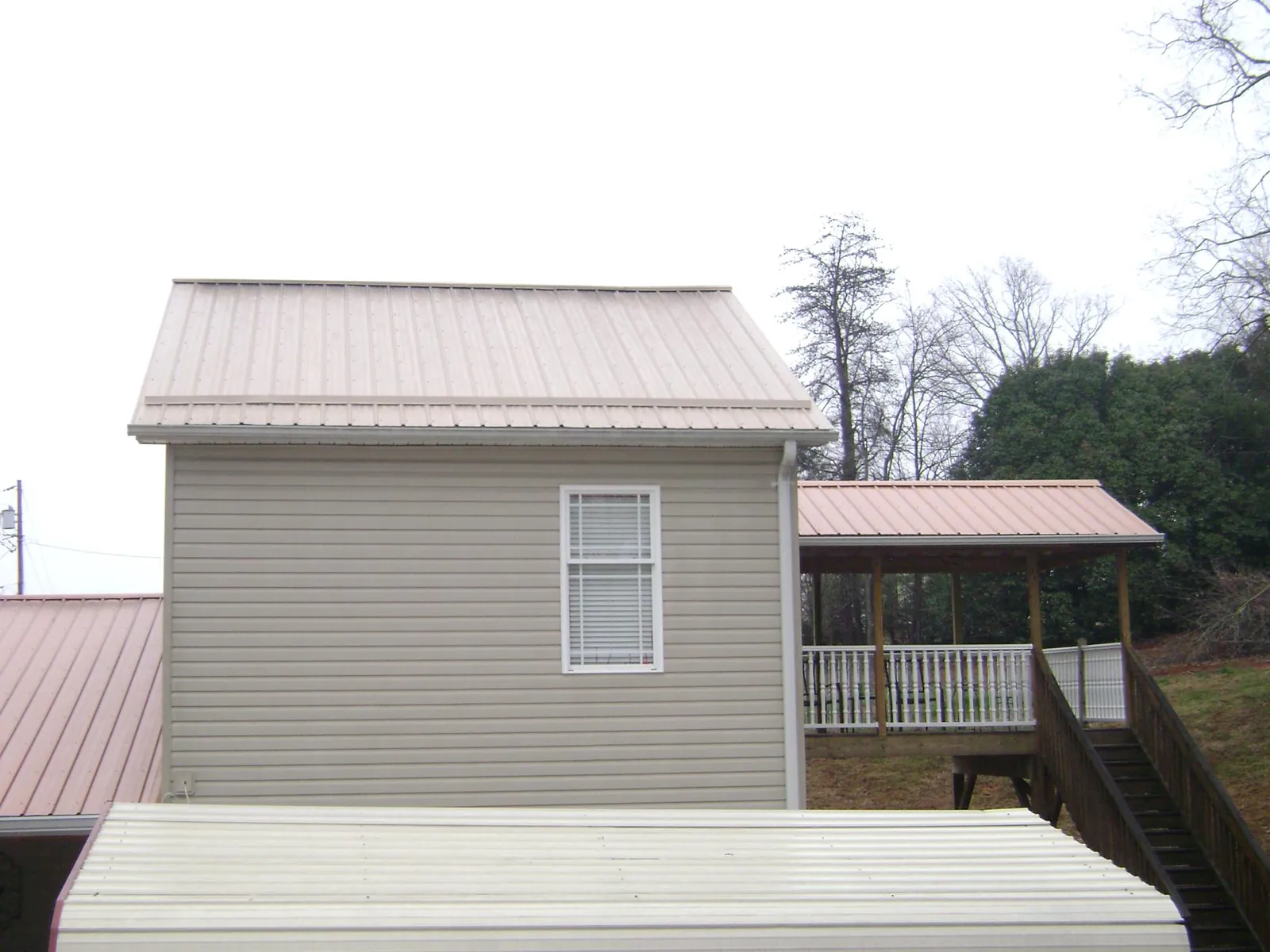 Tan metal roofs on a two story addition and attached porch, from a Roof Replacement job in Rex
